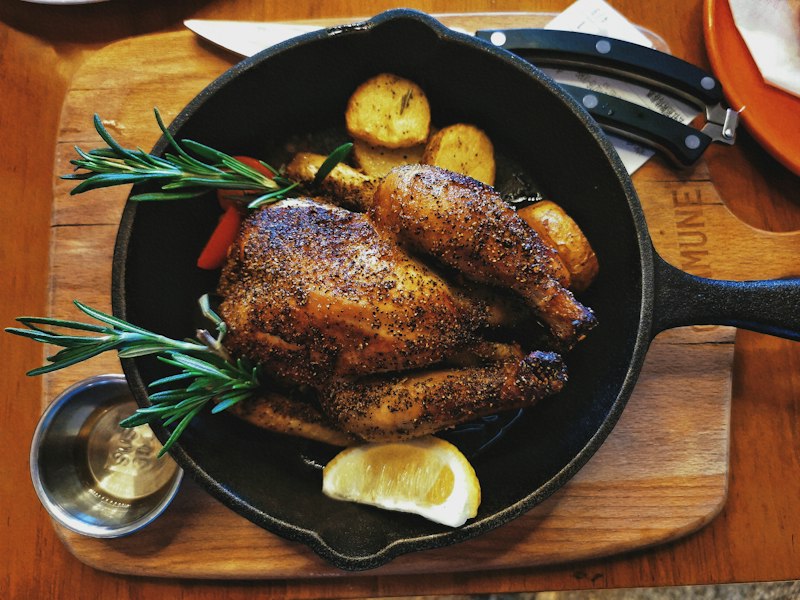 Roasted chicken with potatoes, rosemary and lemon in a black skillet on a wooden table