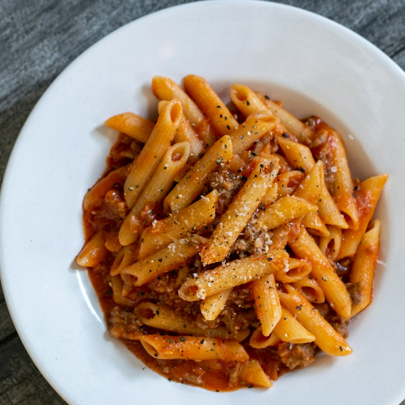 Penne pasta in a rich sauce with grated cheese in a white bowl